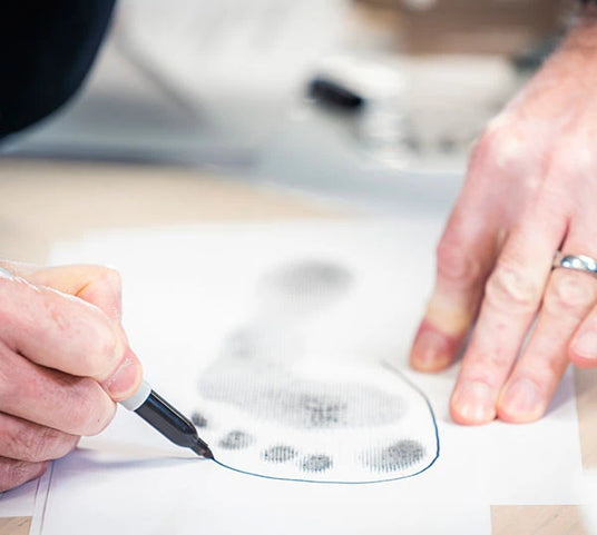 Gros plan d'une personne traçant le contour d'une empreinte de pied sur une feuille de papier avec un stylo