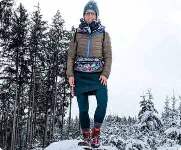 Smiling woman in winter clothing on snowy mountain with raised arm
