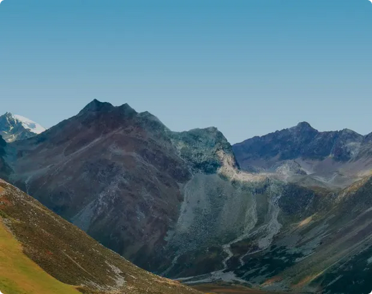 Paysage alpin avec un sentier traversant des collines vertes et rocheuses, sous un ciel bleu dégagé