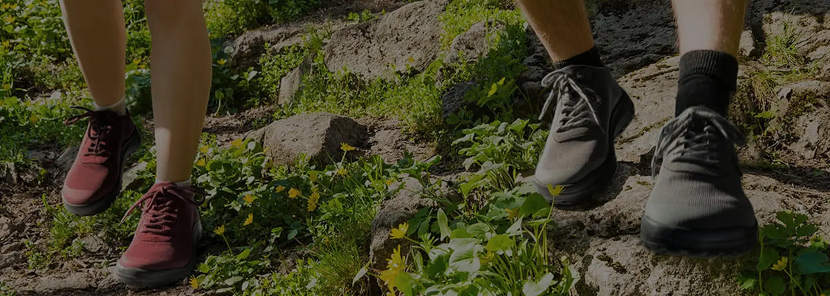 Two people in hiking boots on a rocky, blooming trail