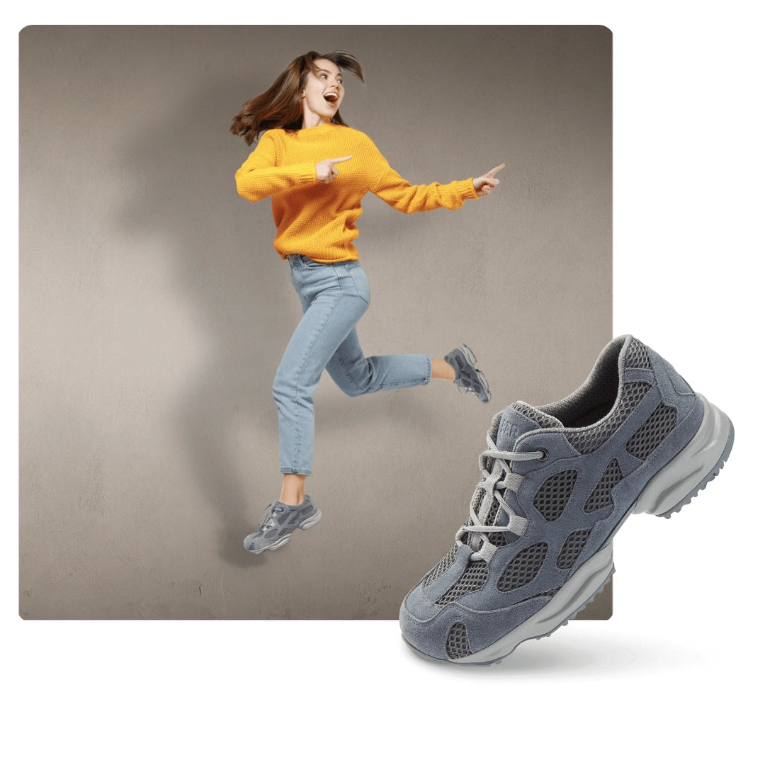 Frau in gelbem Pullover und blauen Jeans springt freudig in grauen Sneakern