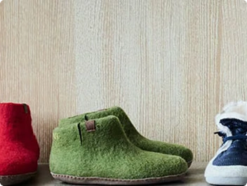 Three pairs of heated felt slippers in red, green, and blue in front of a wooden wall. Perfect for cold winter evenings.