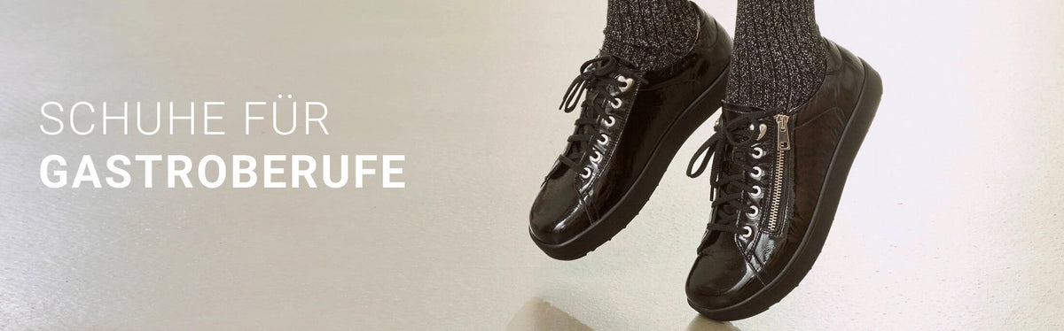 Werbebanner für Schuhe für Gastronomieberufe: Zwei schwarze, glänzende Damenschuhe mit Schnürsenkeln und seitlichem Reißverschluss sind an den Füßen einer Frau mit schwarzen Socken zu sehen. Links steht der Text ‚Schuhe für Gastroberufe‘