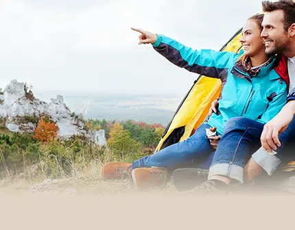 Smiling couple sitting in front of tent in the mountains, looking into the distance. Text: The mountains are calling! BÄR hiking shoe buying guide.