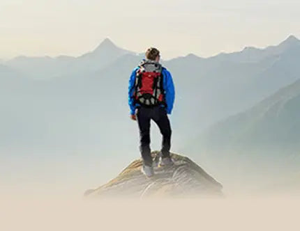 Person on mountain ridge with sturdy hiking boot, surrounded by mountains and blue sky. Text: Feel Free