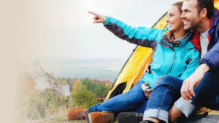 Smiling couple sitting in front of tent in the mountains, looking into the distance. Text: The mountains are calling! BÄR hiking shoe buying guide.