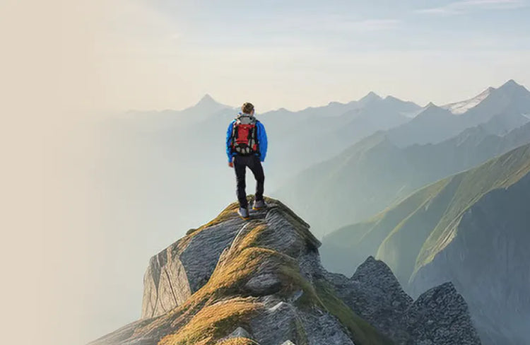 Person on mountain ridge with sturdy hiking boot, surrounded by mountains and blue sky. Text: Feel Free