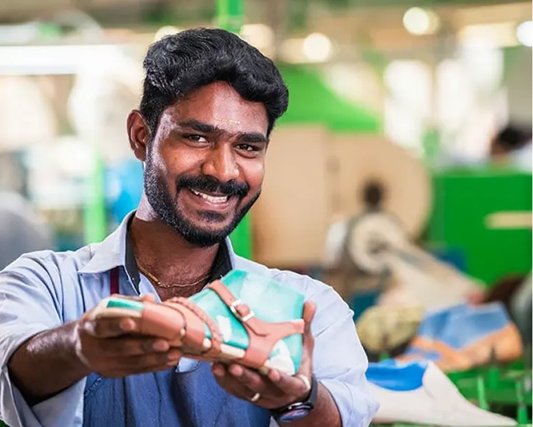 Un homme souriant dans une usine présente fièrement une chaussure fabriquée.