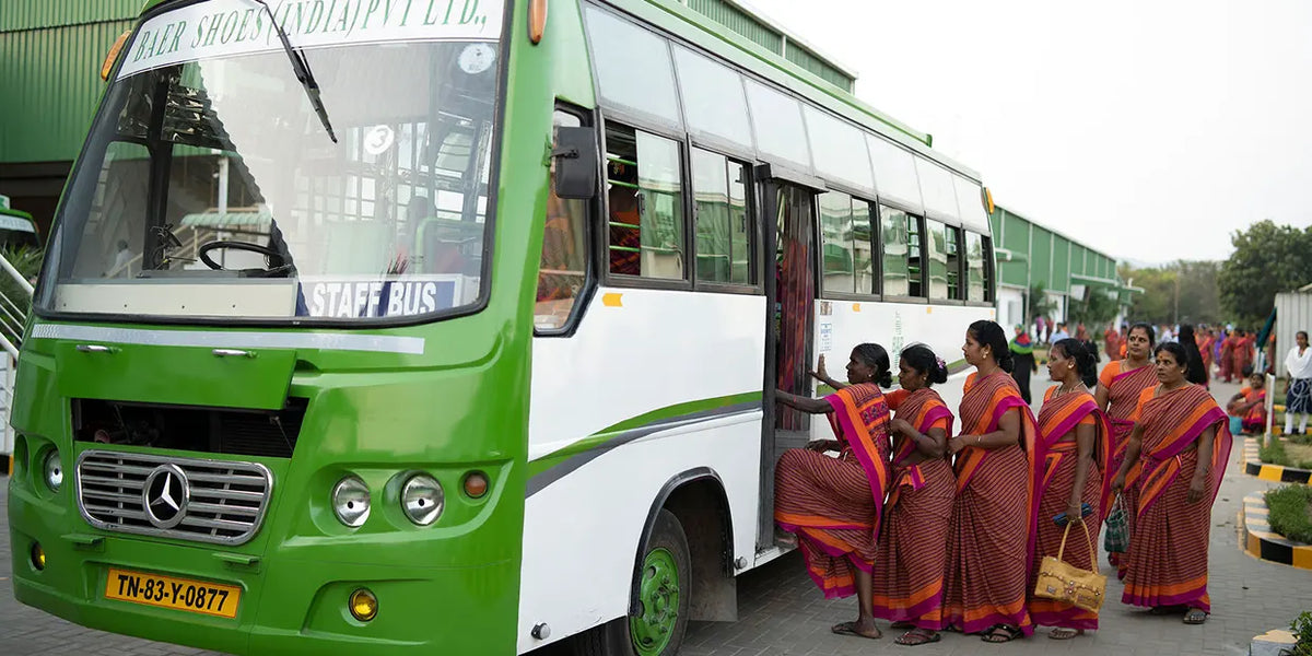 Groupe de femmes en saris traditionnels montant dans un bus d'entreprise vert devant une usine
