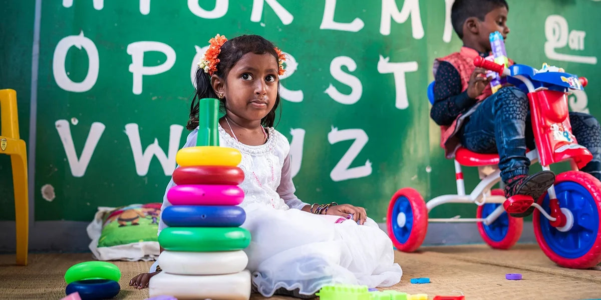 Un enfant assis par terre à la maternelle joue avec des jouets colorés. En arrière-plan, un mur vert avec des lettres peintes.
