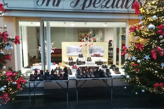 Schaufenster eines Schuhgeschäfts mit Weihnachtsdekoration und Tischen voller Schuhe