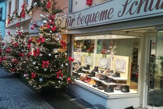 Ein festlich geschmücktes Schuhgeschäft mit Weihnachtsbäumen und Lichtern in der Auslage. Außenansicht eines Schuhladens mit dekorierten Schaufenstern.