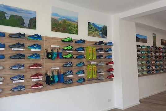 Wand mit diversen Sportschuhen und Zubehör in einem modernen Geschäft, dekoriert mit Landschaftsfotografien.